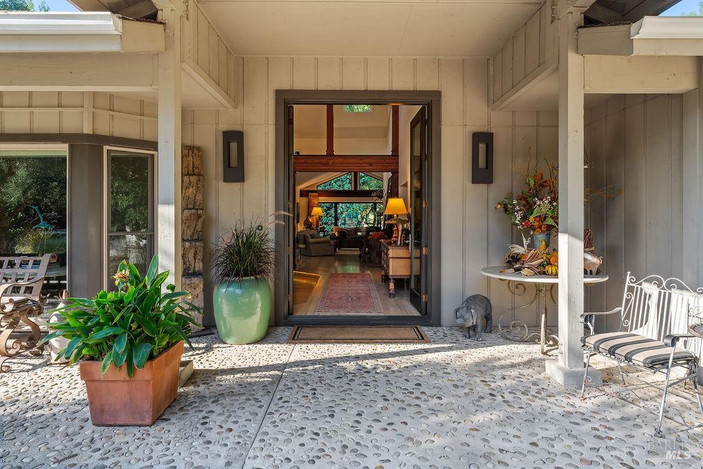 Covered front porch with pebble-stone flooring, potted plants, and open doors to a furnished living room.