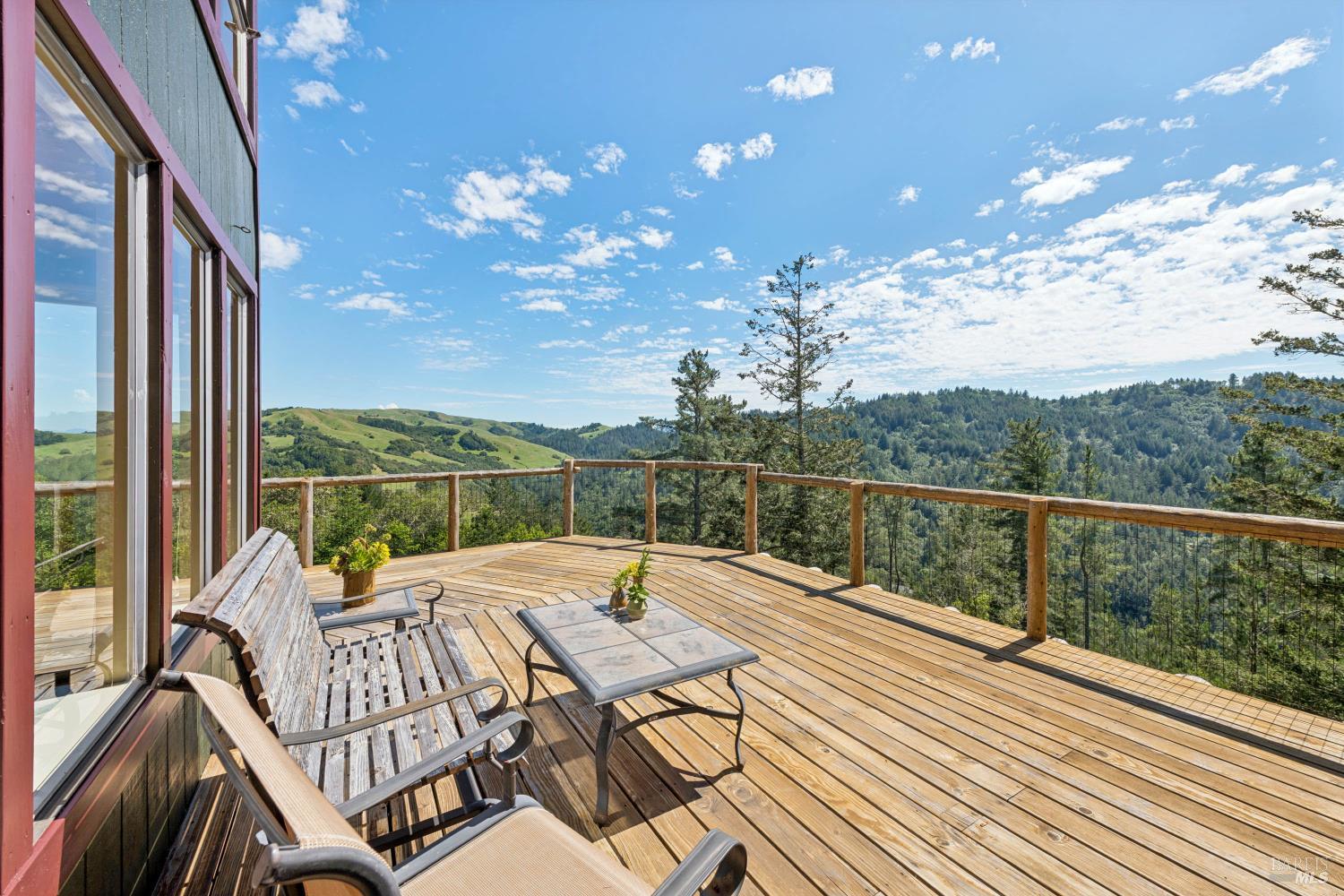 Wooden deck with lounge chairs overlooking green hills and forested ridges.