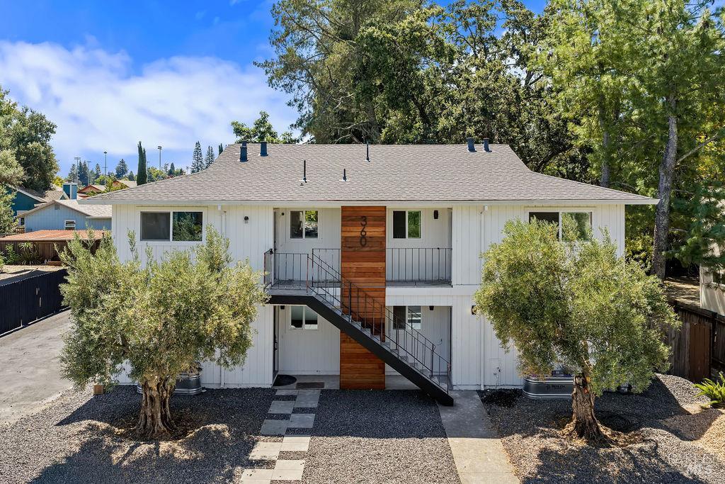 White two-story home with wood accents, exterior stairs, gravel landscaping, and two small trees.