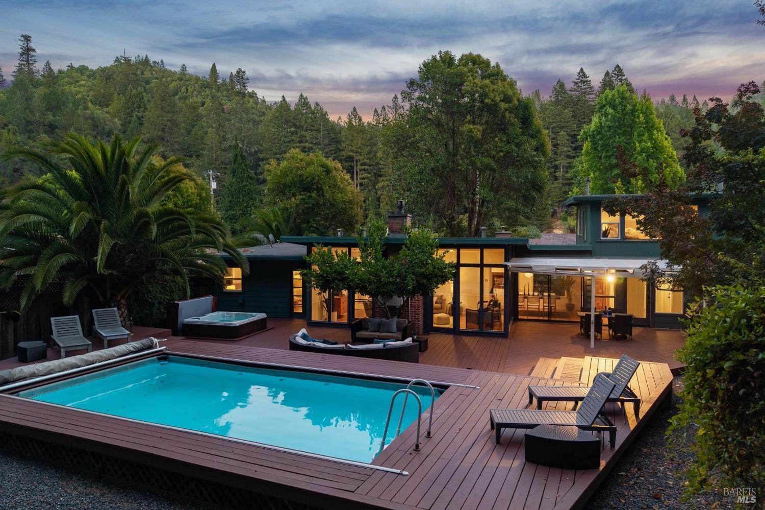Modern home with a pool and hot tub on a wooded hillside at dusk.