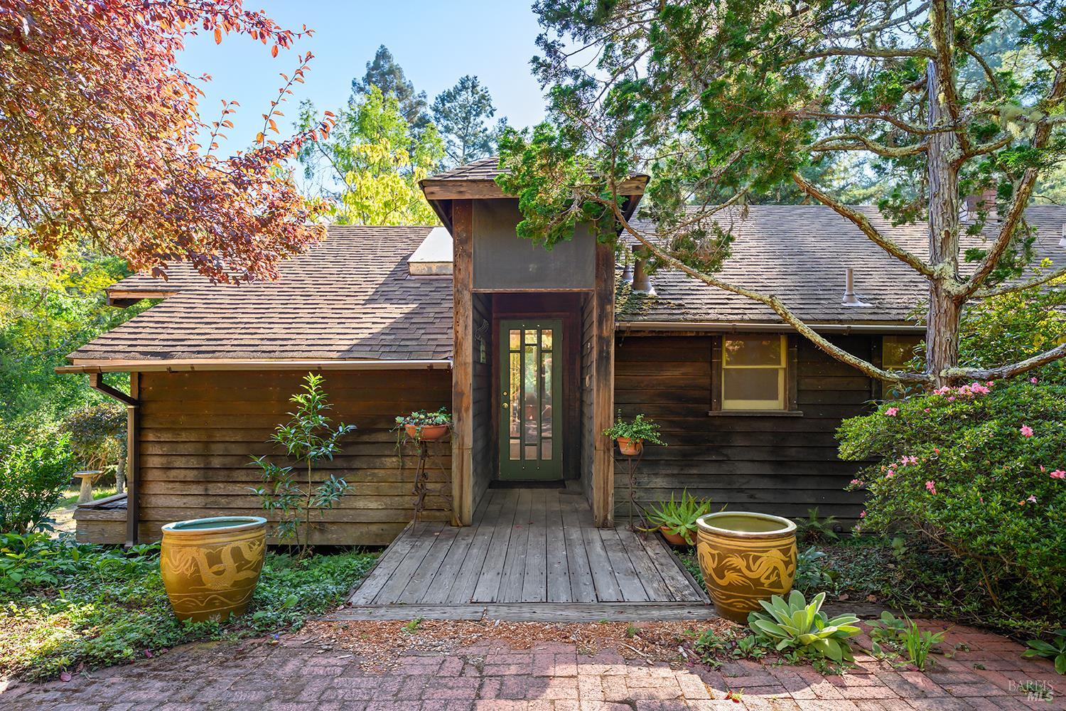 Wood-sided home with a tall central entry, wooden walkway, and mature garden landscaping.