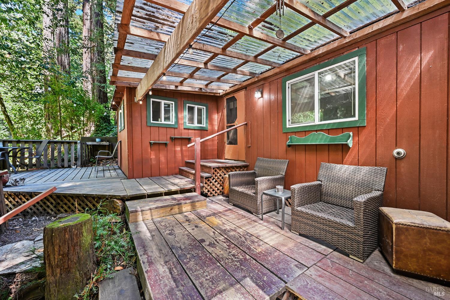 Outdoor deck beside a red-sided home, with wicker seating under a translucent roof.