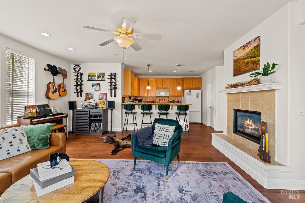 Open-plan living room with teal armchair, tiled fireplace, guitars on the wall, and a dog on the floor.