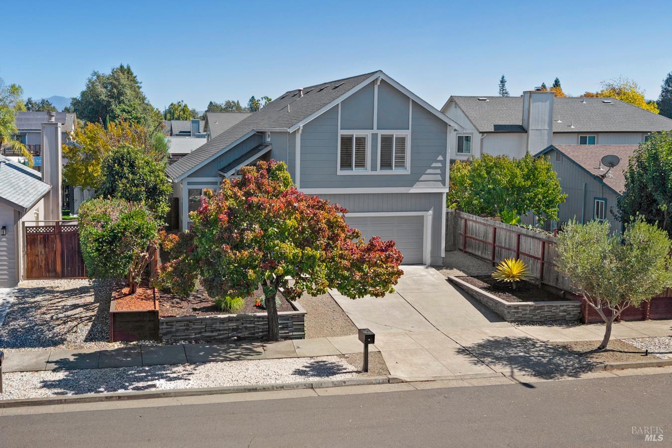 Two-story gray house with a front-facing garage, concrete driveway, and colorful autumn trees.