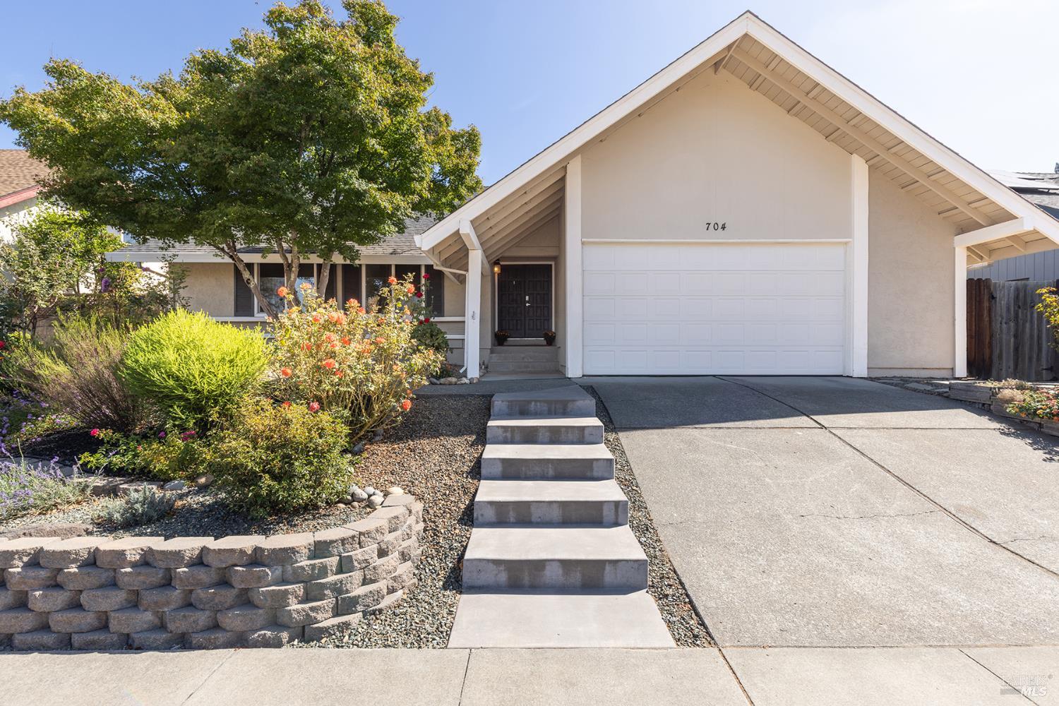 Single-story home with a white gabled garage, front steps, and landscaped garden.