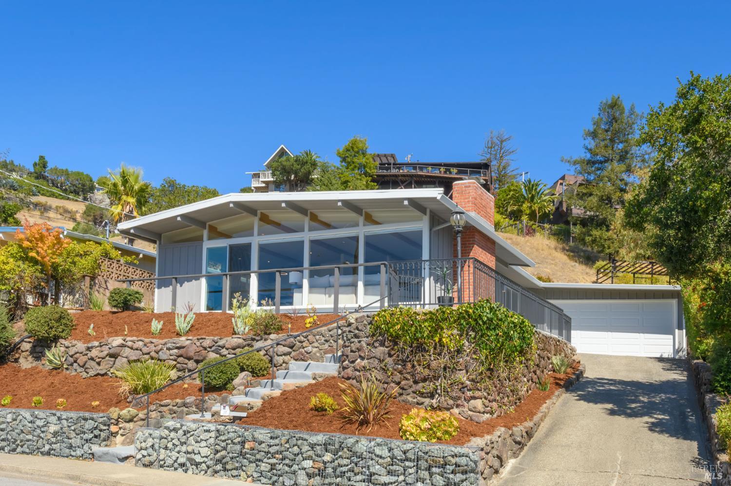 Modern hillside home with a broad glass façade, terraced gardens, and an attached garage.