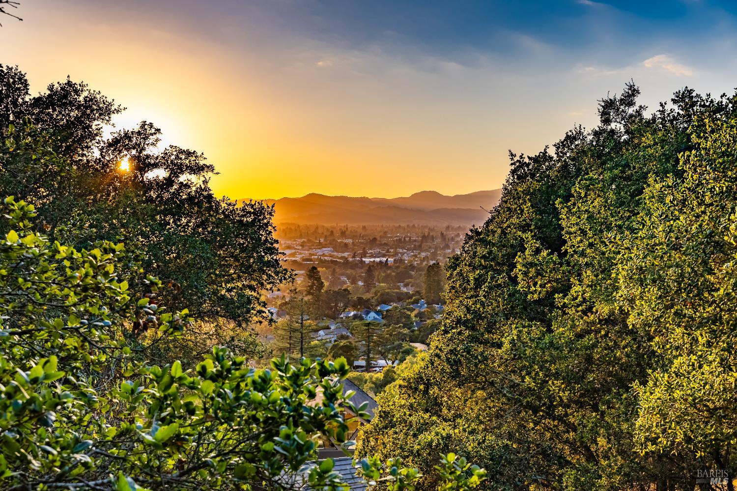 Sunset over a wooded residential valley with distant mountain ridges.