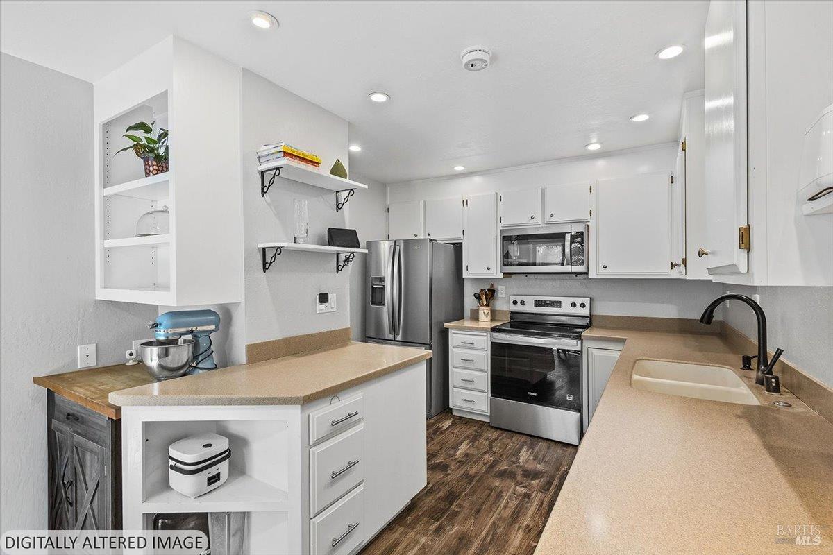 Kitchen with white cabinetry, beige counters, stainless appliances, and a peninsula with a blue stand mixer.