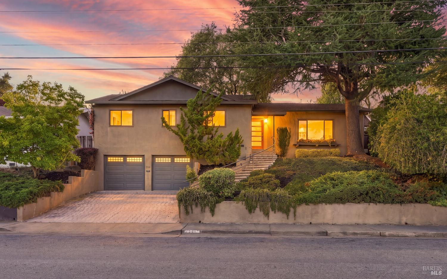Two-story stucco home with a double garage and illuminated windows at dusk.