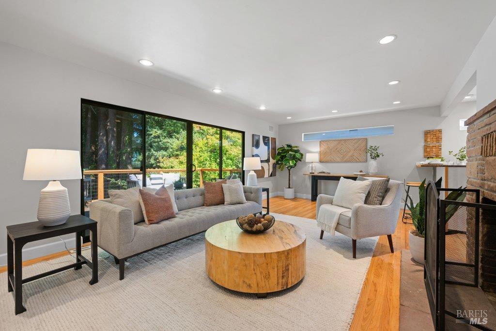Staged living room with large windows overlooking trees and a brick fireplace.
