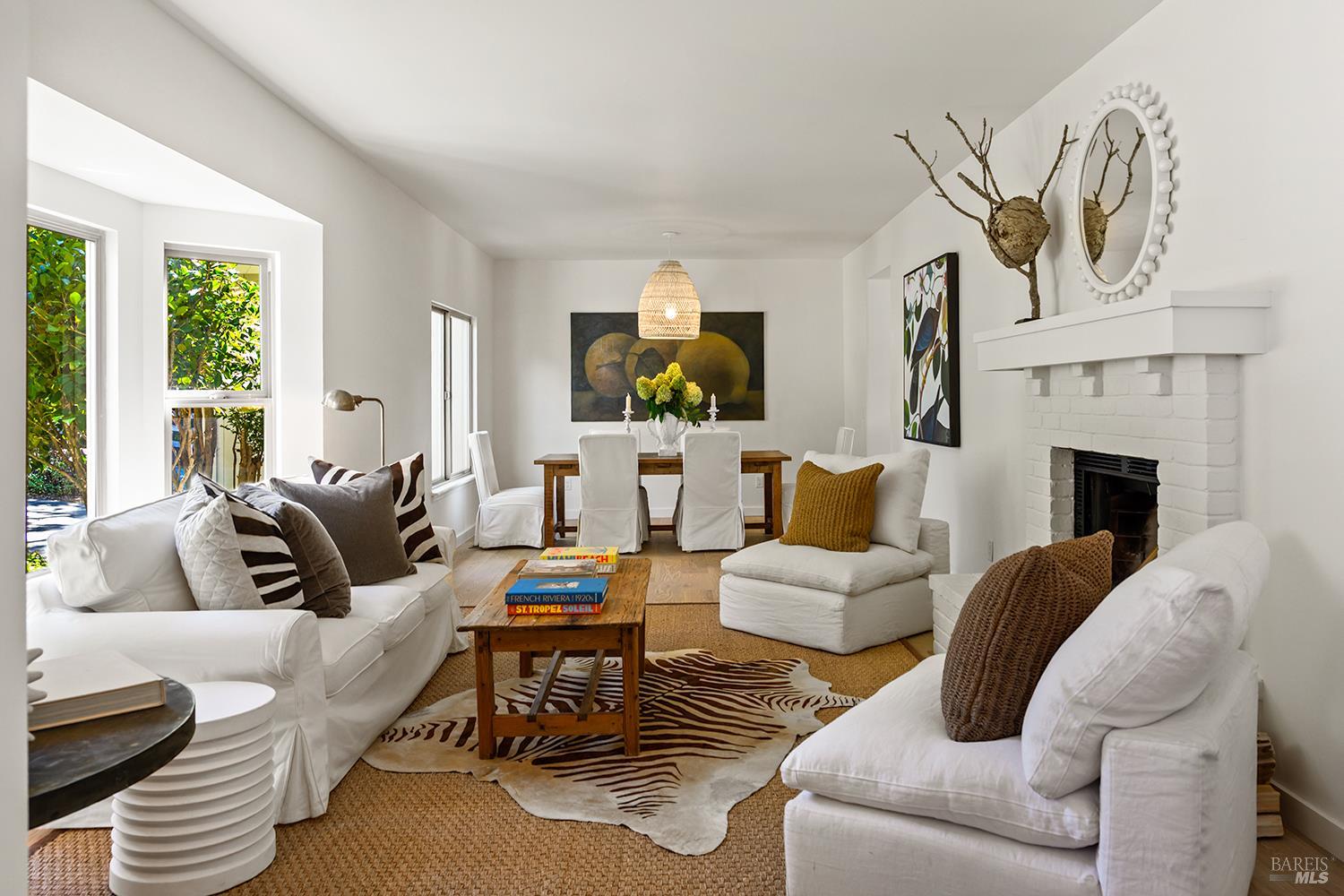 Bright living room with white sofas, a brick fireplace, and an adjoining dining area.