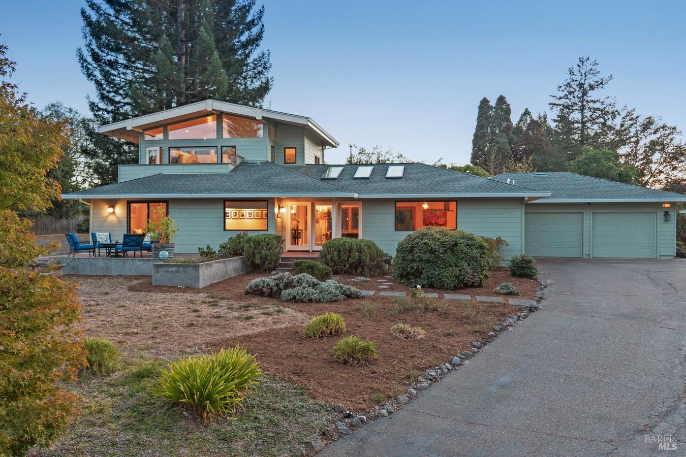 Modern home with a raised upper level, two-car garage, and landscaped front yard at dusk.