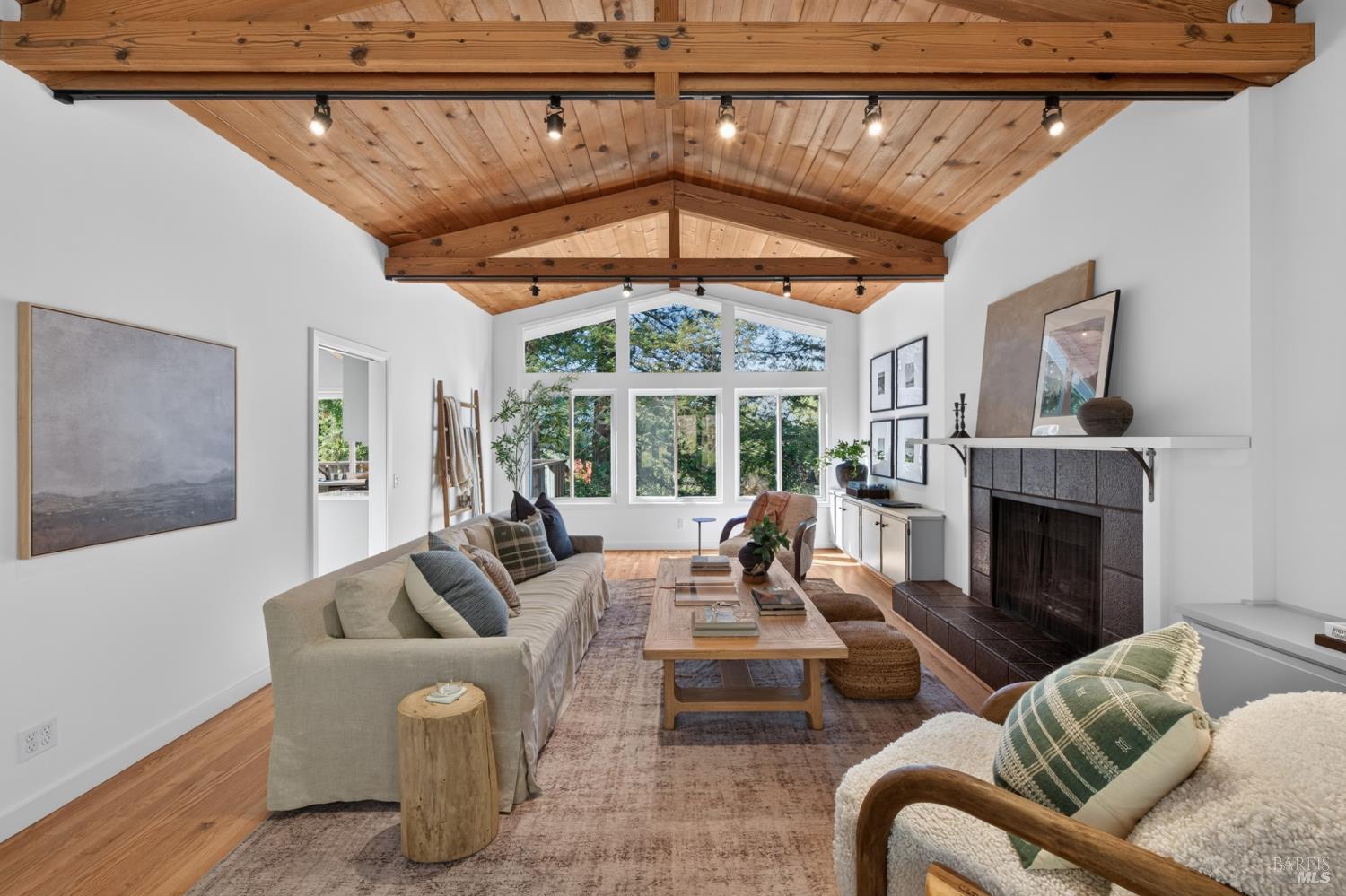 Living room with a vaulted wood ceiling, exposed beams, large windows, and a tiled fireplace.