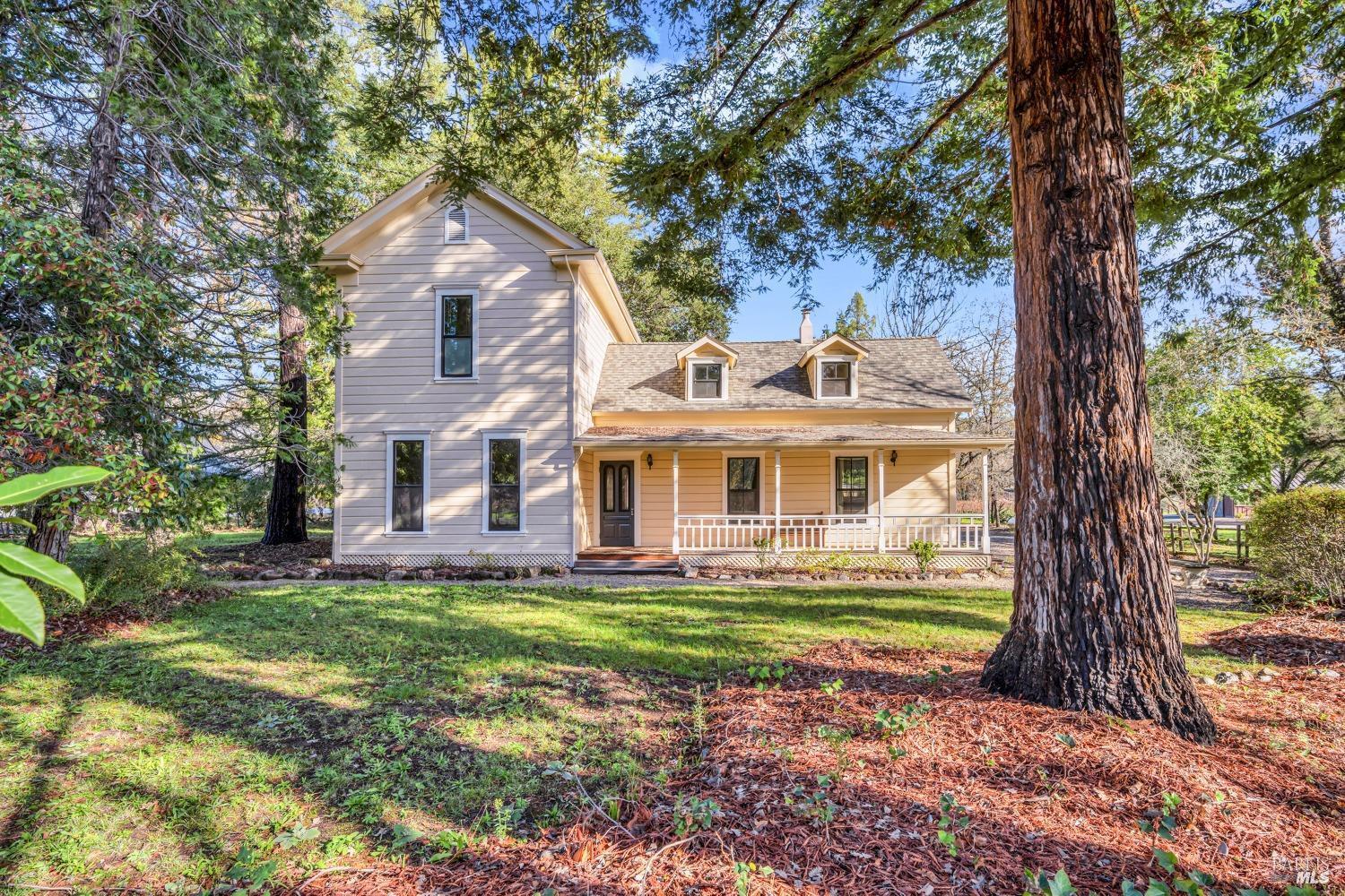 Two-story house with a covered porch, set among mature trees and a grassy yard.