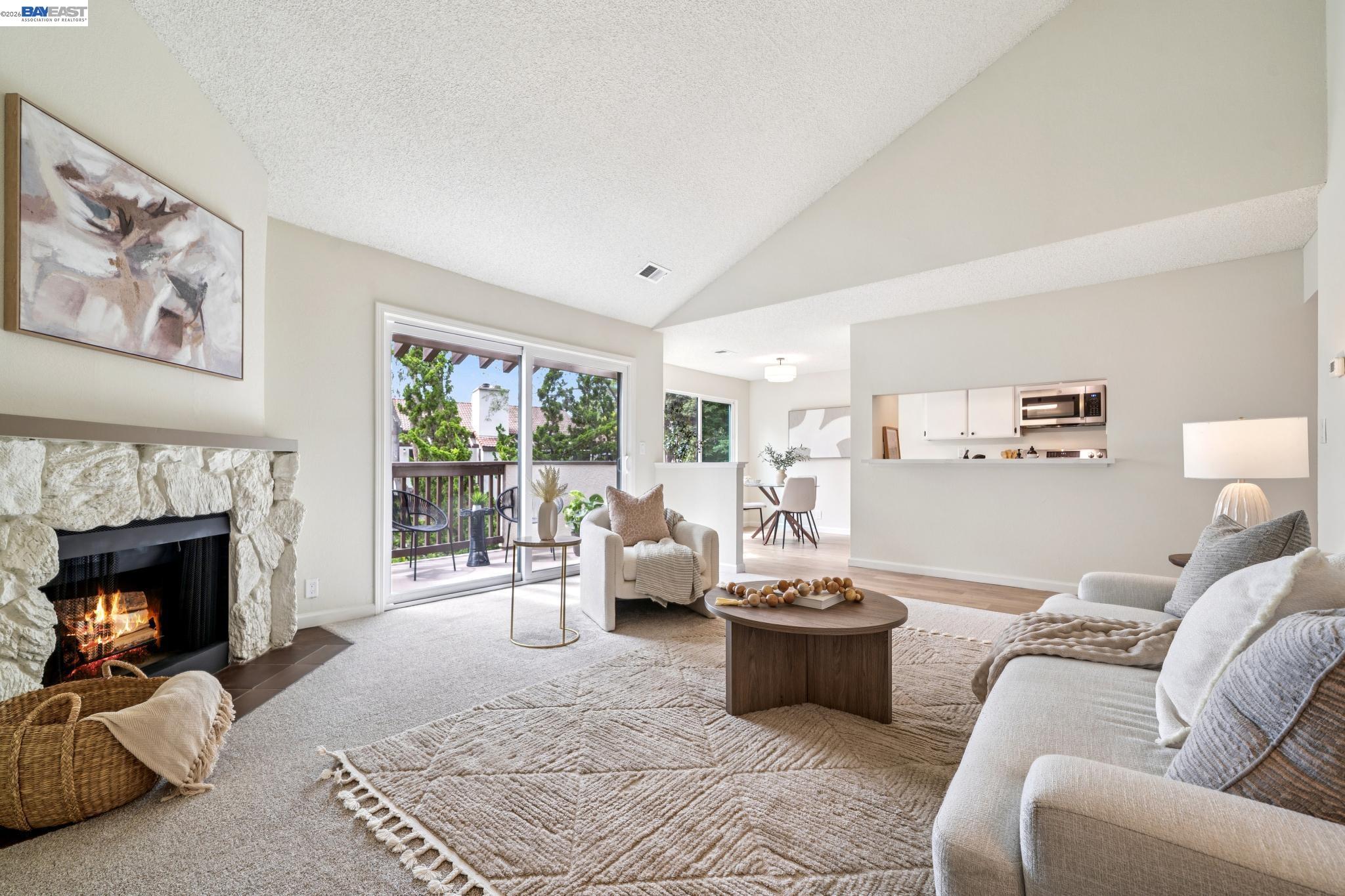 Staged living room with a stone fireplace, vaulted ceiling, and sliding glass door to a balcony.