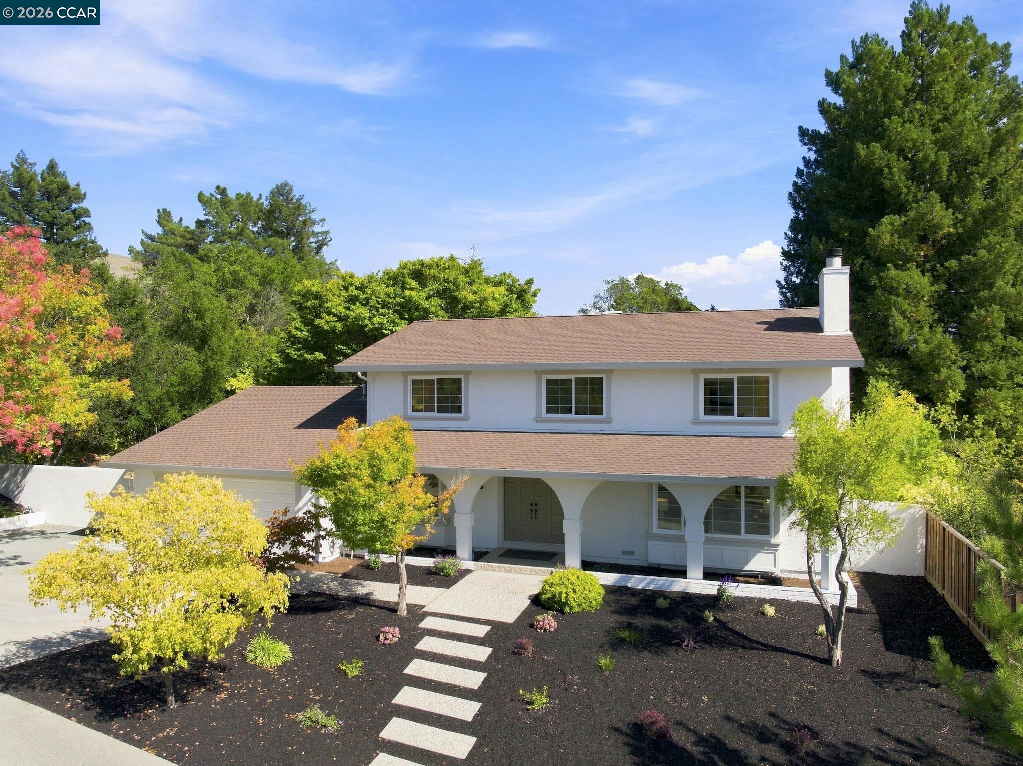 White two-story house with an arched covered porch and landscaped front yard.