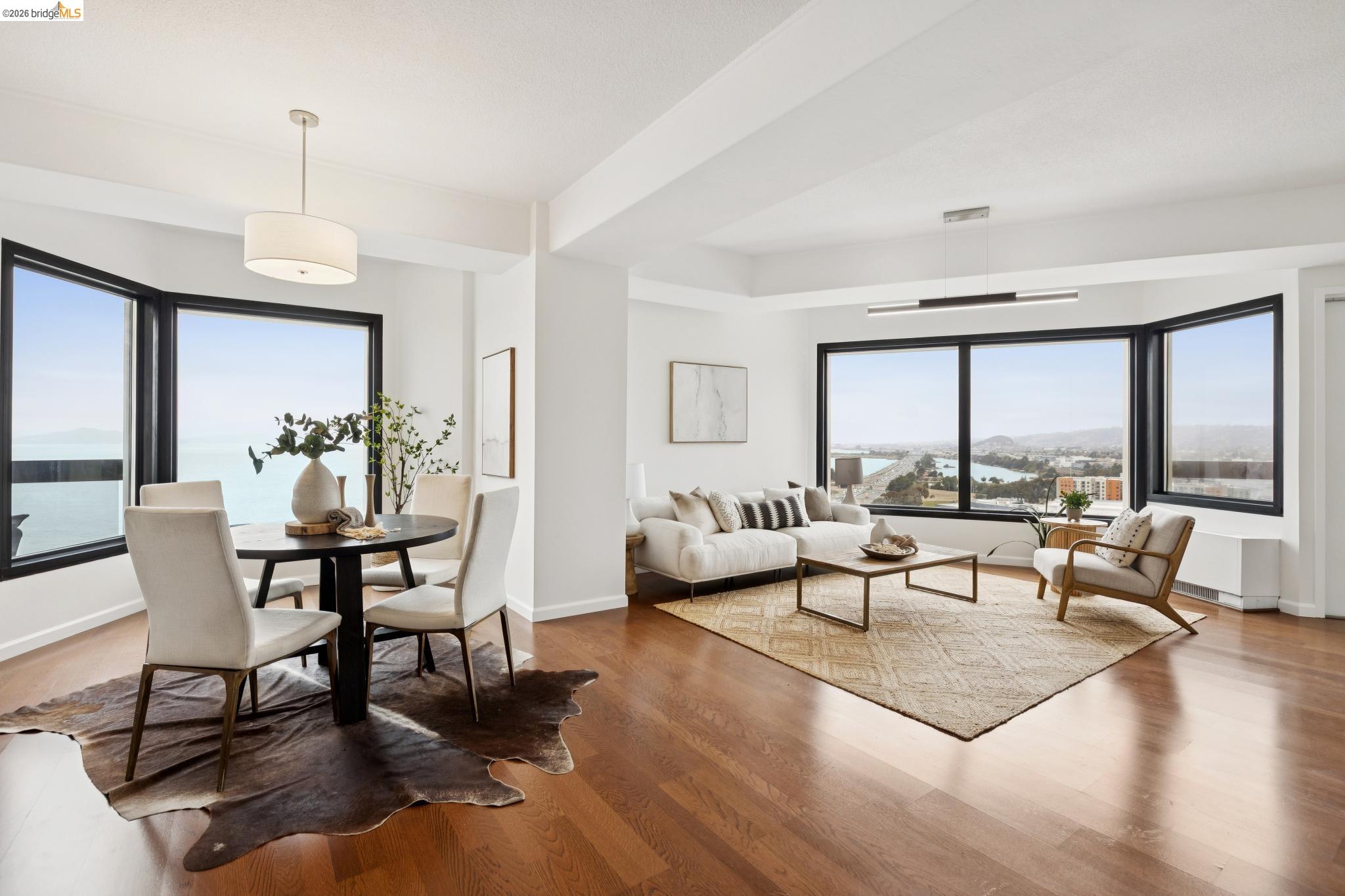 Open-plan living and dining room with hardwood floors and expansive windows overlooking the water.