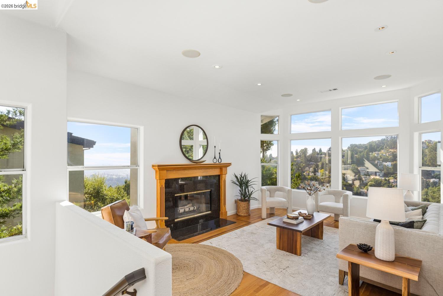 Bright living room with a wood-trimmed fireplace, large hillside-view windows, and neutral furnishings.