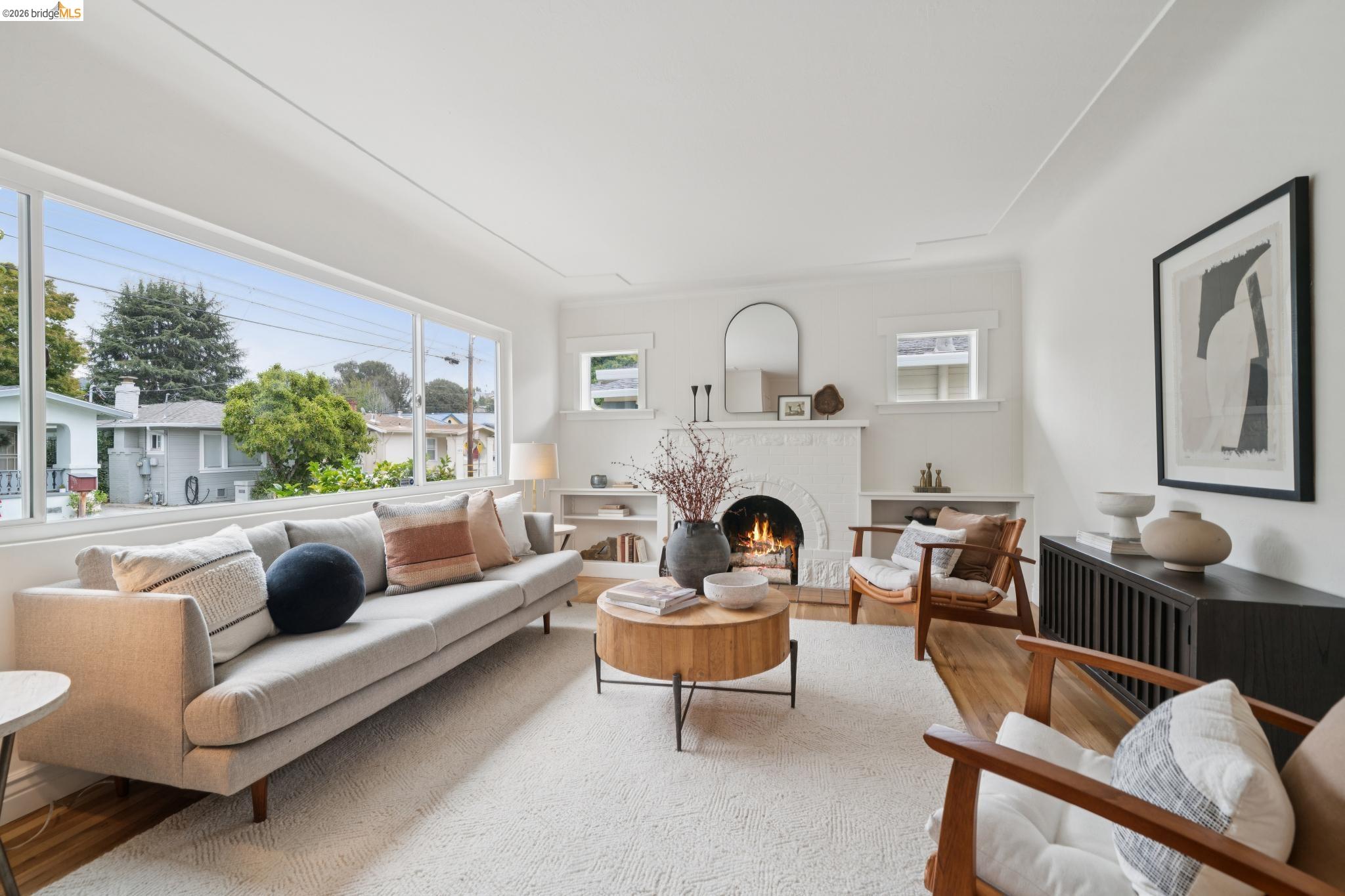 Staged living room with a white-brick fireplace, lit fire, and broad picture window.