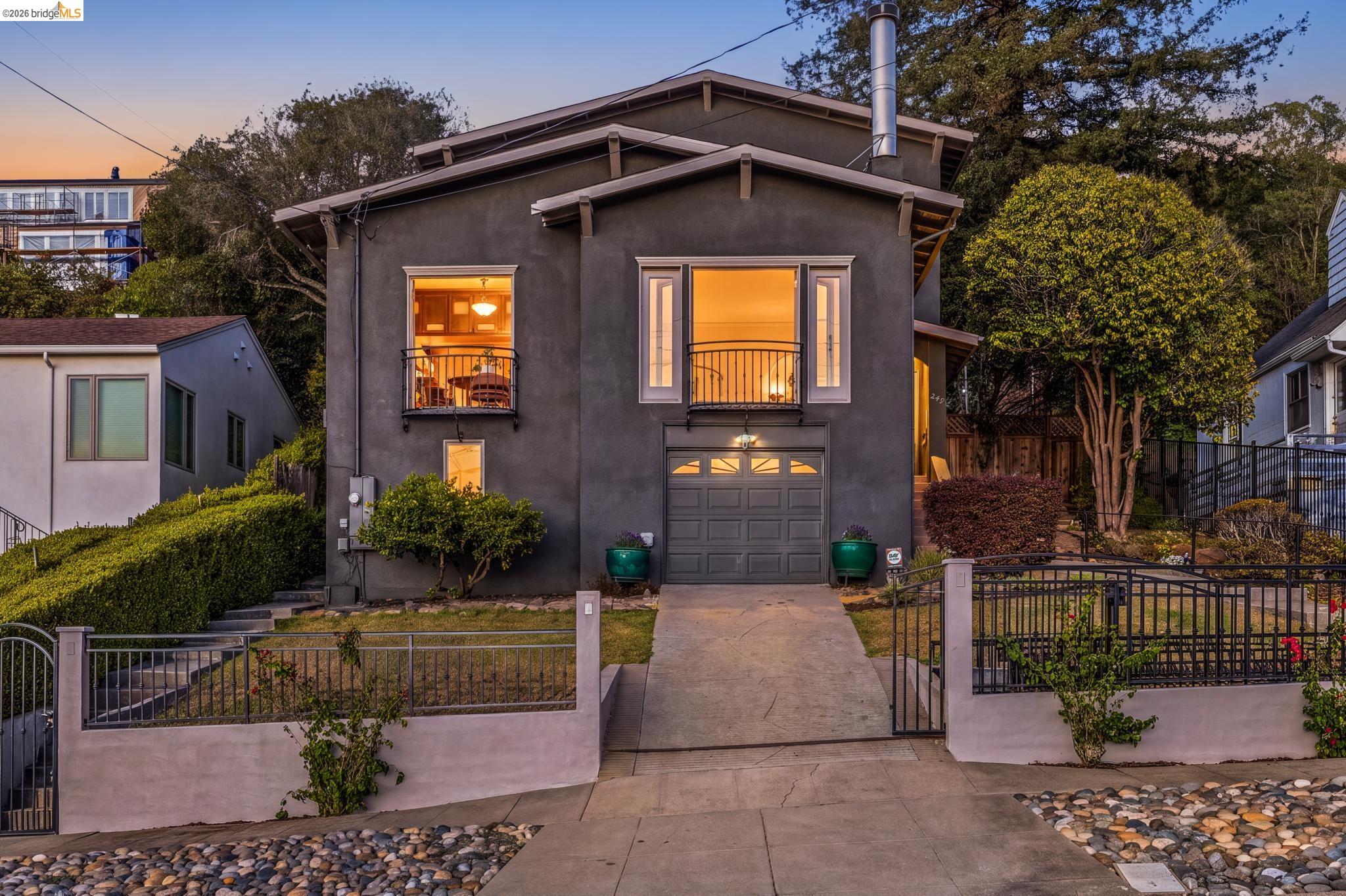 Dark gray two-story home with lit windows, balconies, and a gated driveway at dusk.