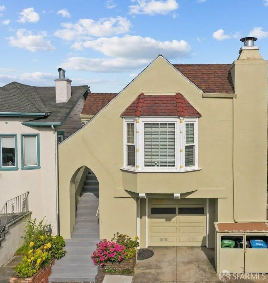 Cream stucco home with a red-tile roof, bay window, and landscaped front steps.