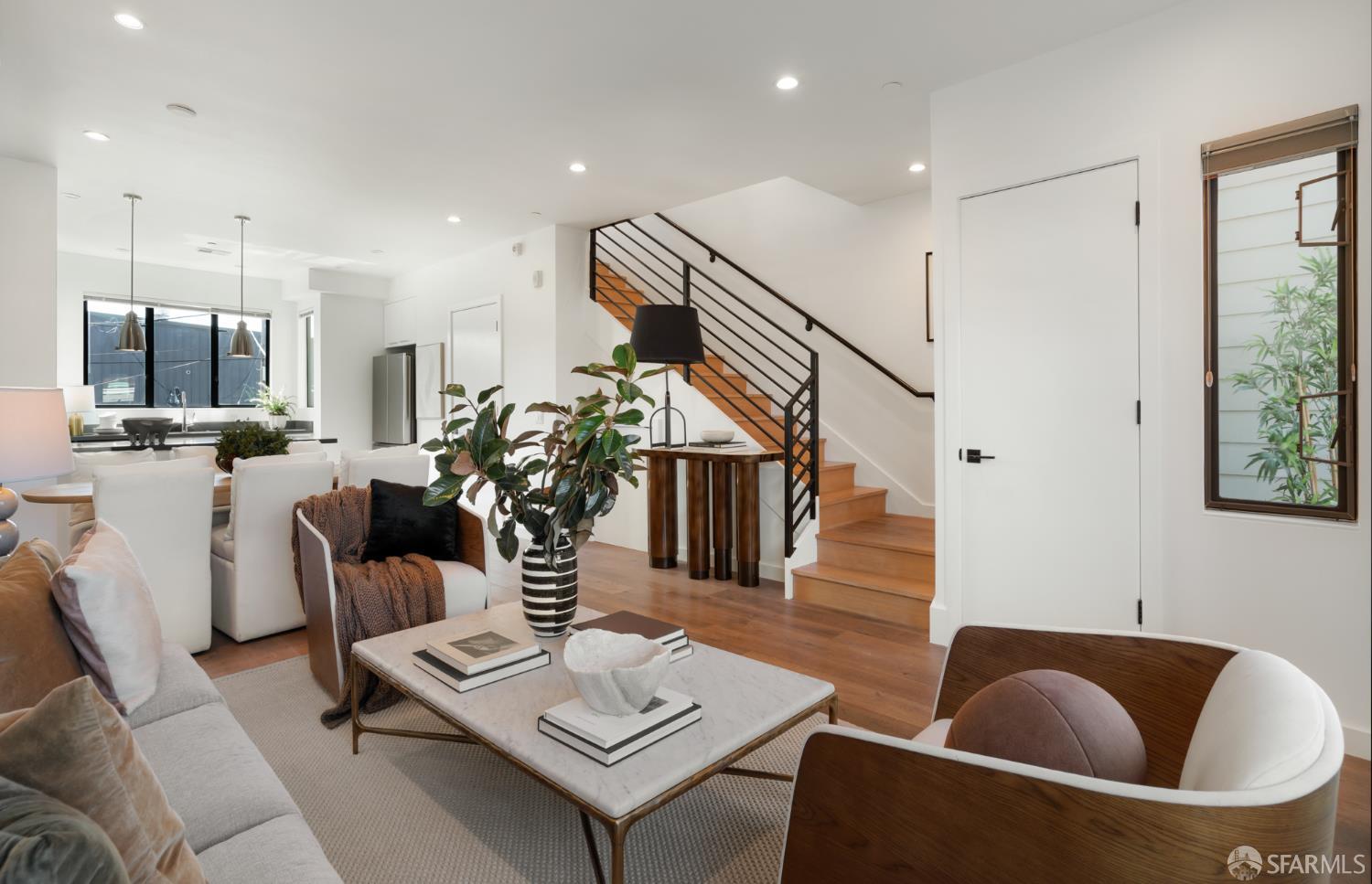 Open-plan living room with white sofas, marble coffee table, and wood staircase.