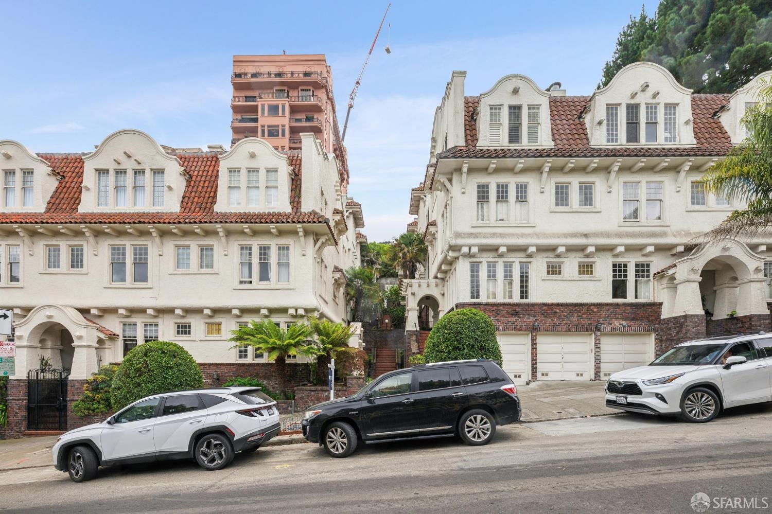 White Spanish Revival residential buildings with red tile roofs, arched entrances, and parked cars along the street.