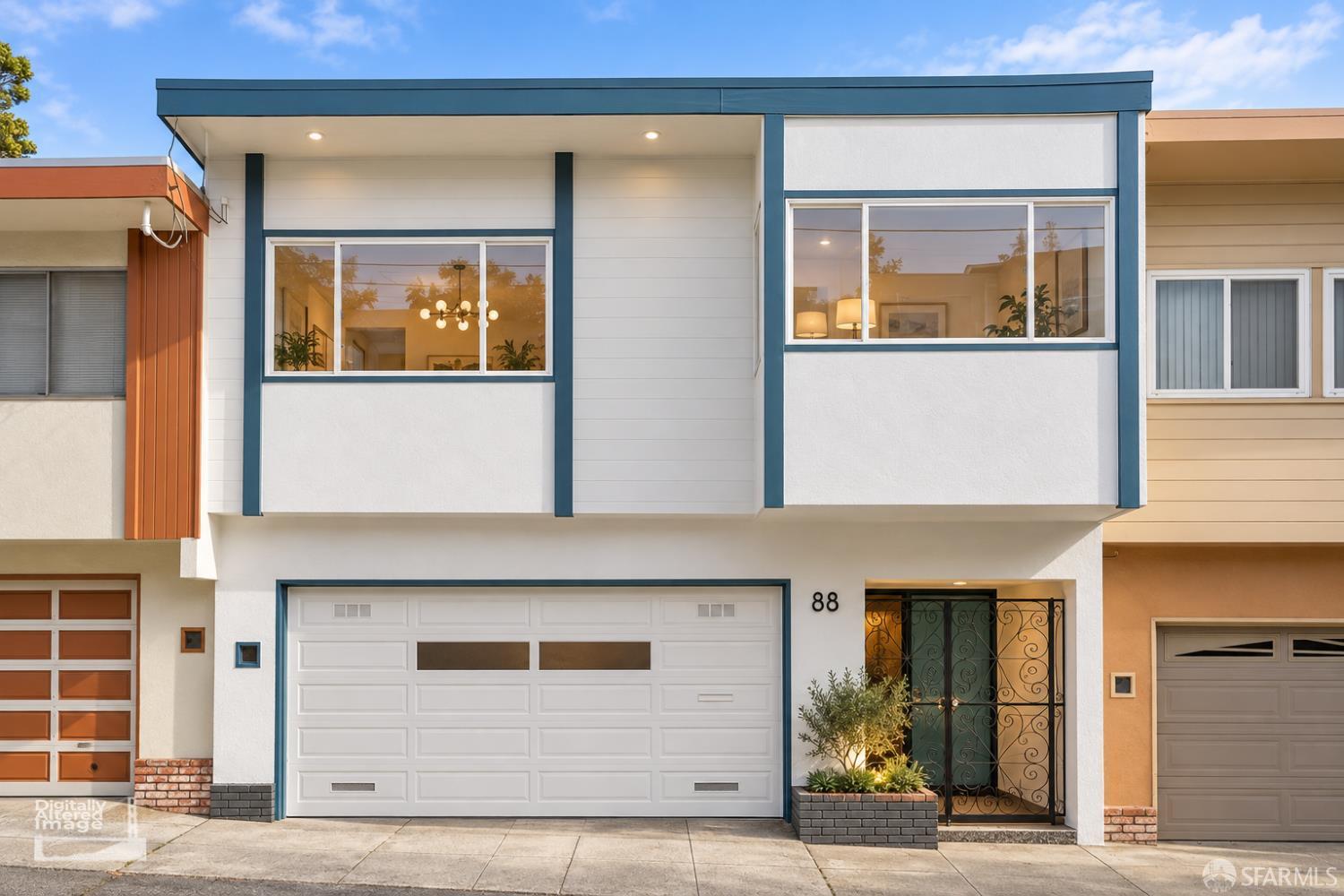Modern white home with blue trim, a wide garage, and a wrought-iron entry gate.