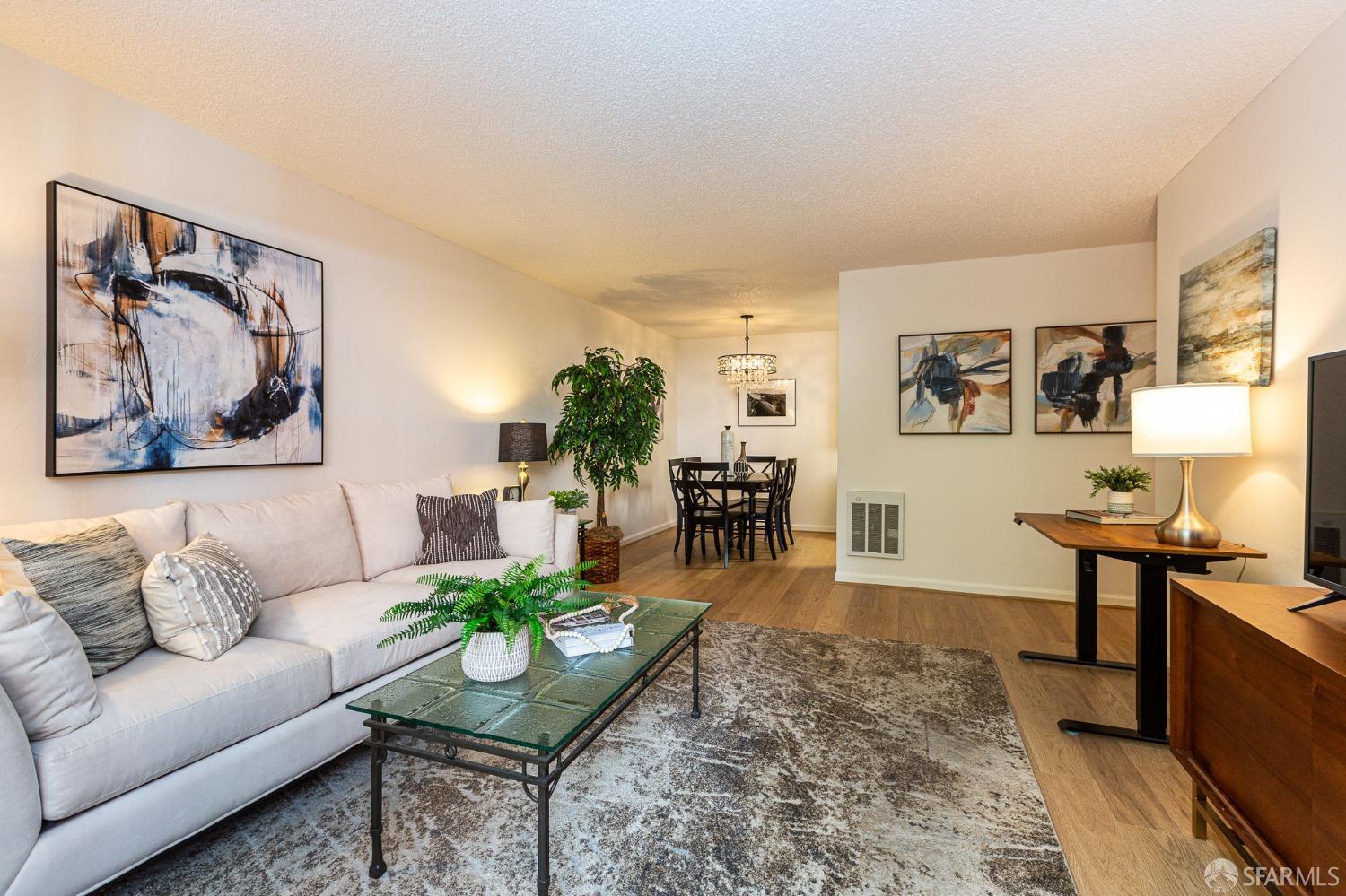 Furnished living room with a light sectional, glass coffee table, and dining area beyond.