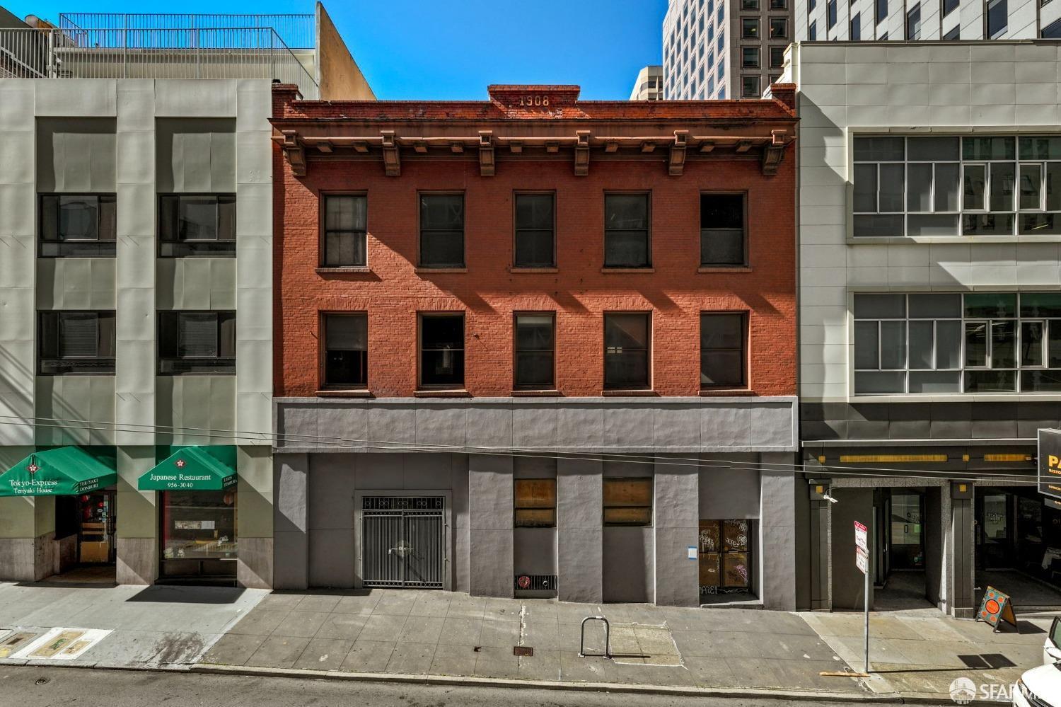 Red-brick commercial building marked 1908, flanked by modern office buildings and restaurant storefronts.
