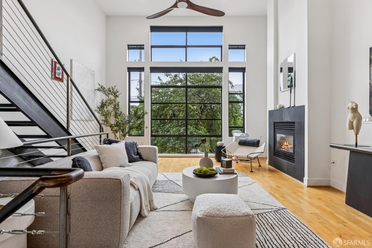 Living room with double-height windows, a black metal staircase, and a modern fireplace.