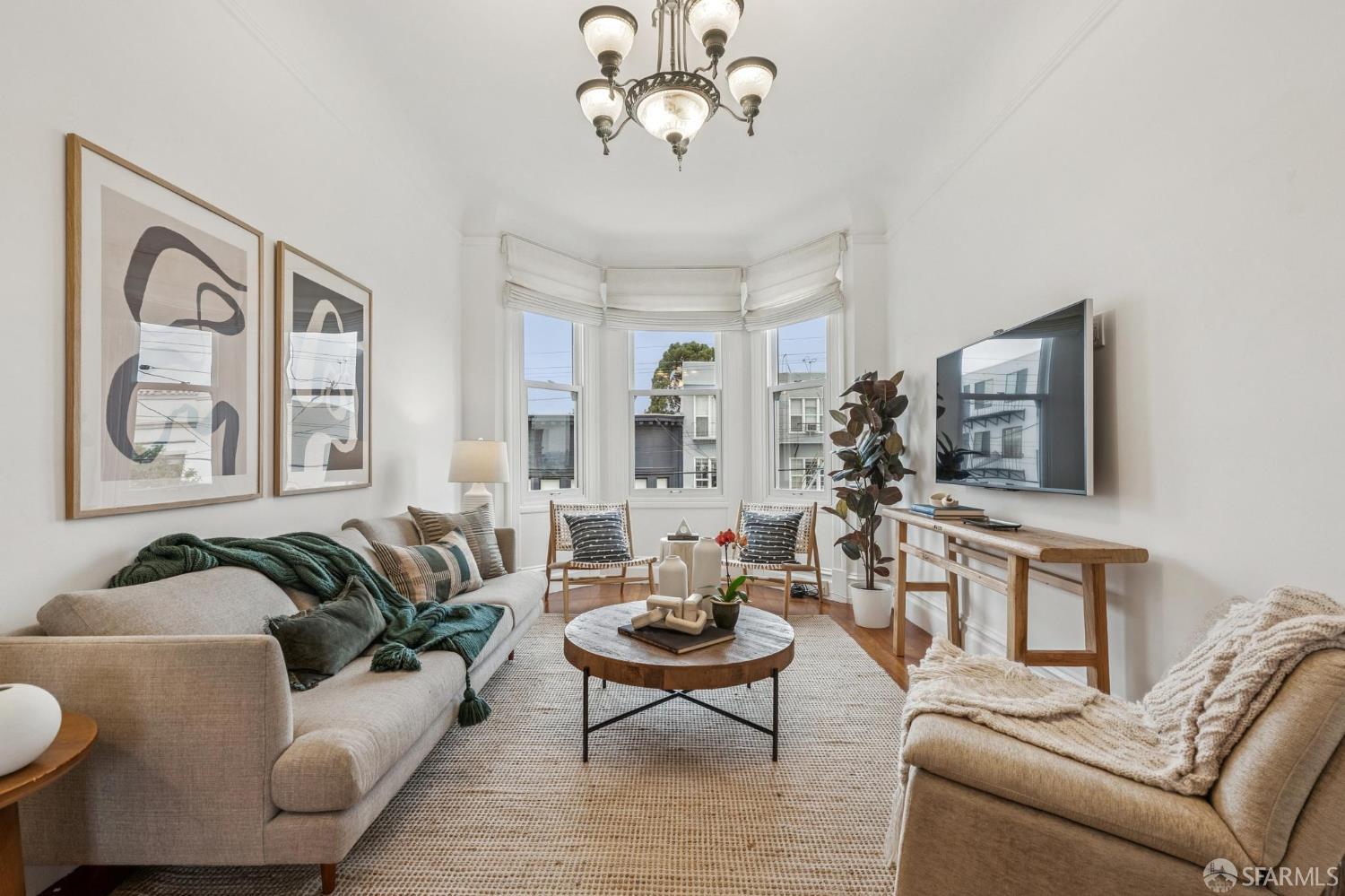Staged living room with a bay window, beige sofas, and a round coffee table.