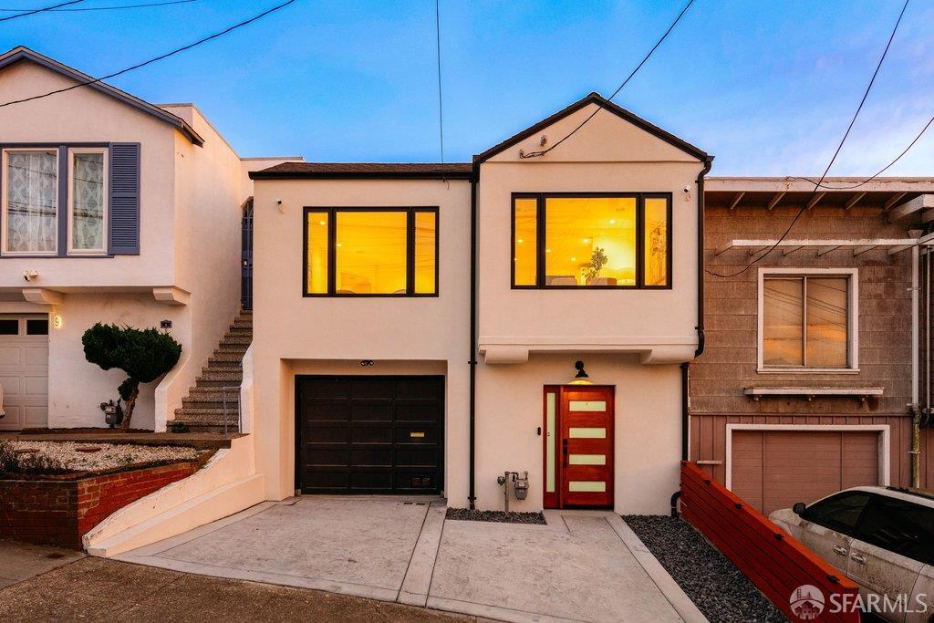 Two-story stucco home with a black garage door, red entry door, and warmly lit upper windows.