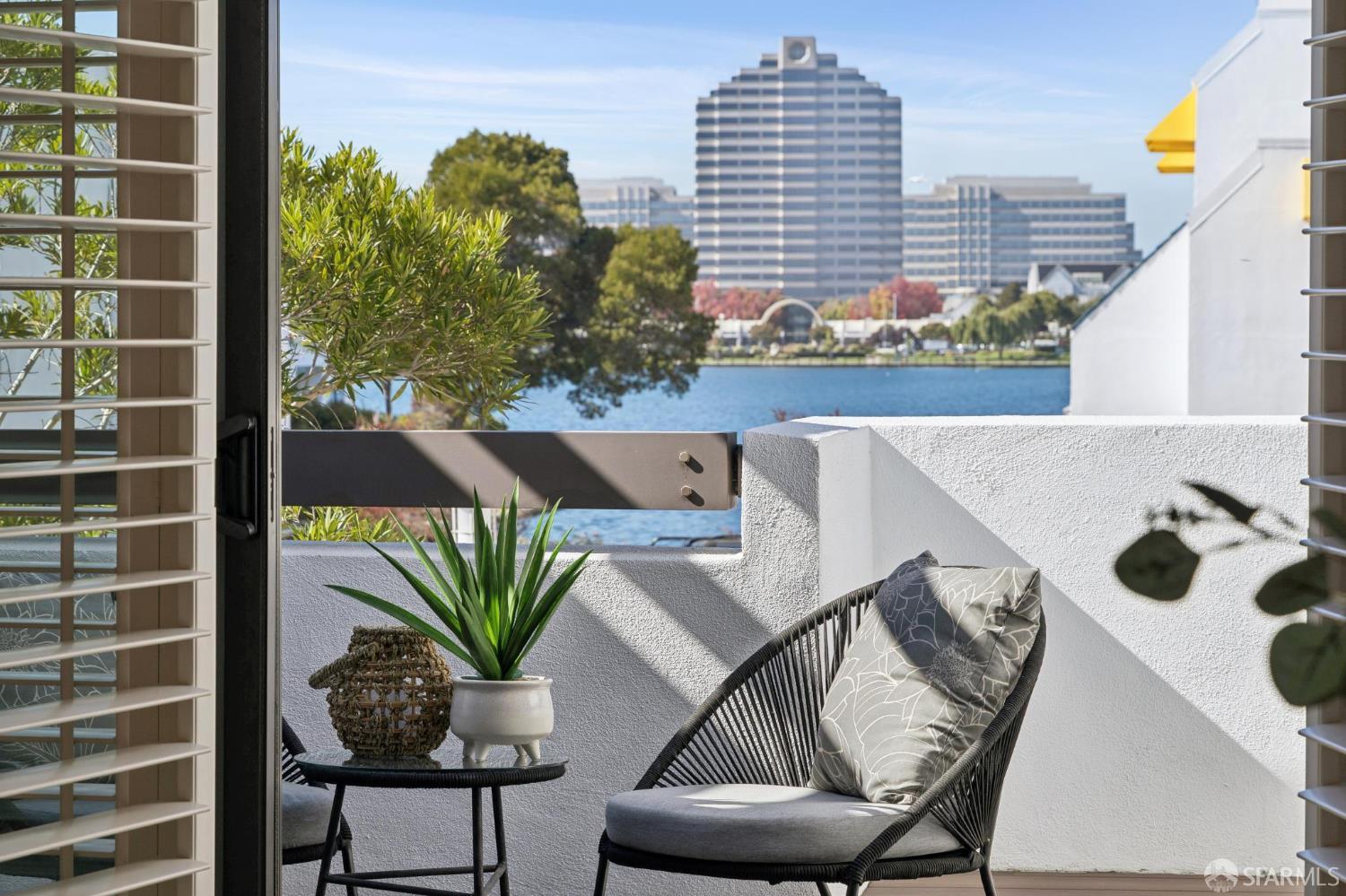 Furnished balcony with a woven lounge chair overlooking the water and city buildings.