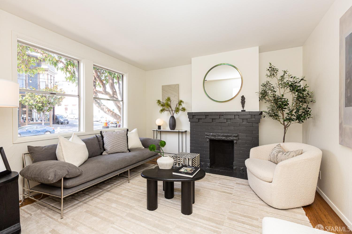 Staged living room with a black brick fireplace, gray sofa, and large windows.