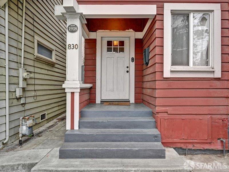Home entrance with a white front door, concrete steps, and red clapboard siding.