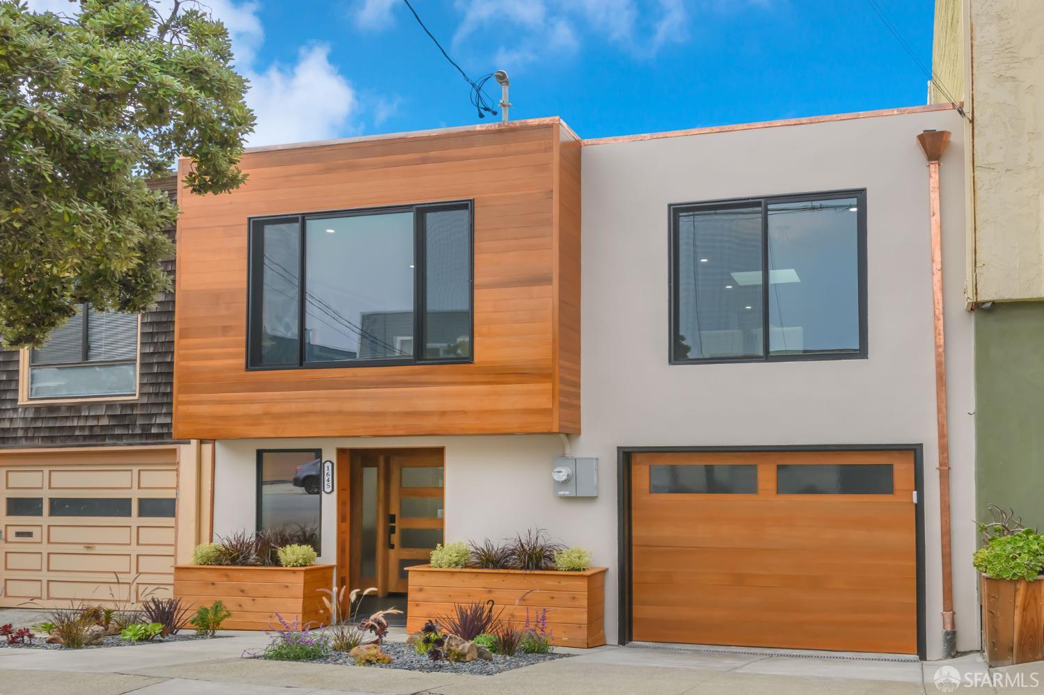 Modern home with warm wood siding, large windows, and a matching wood garage door.