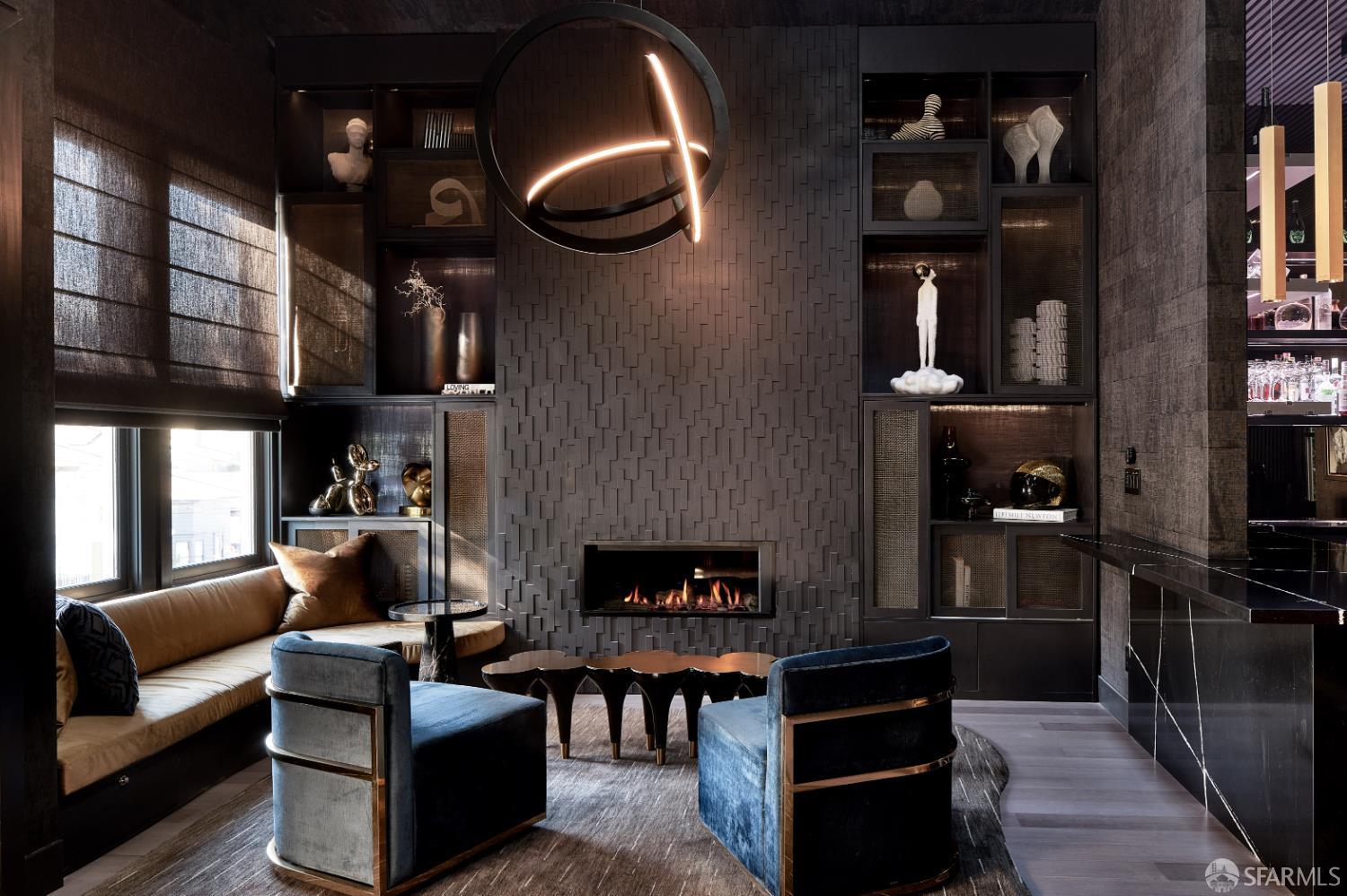 Living room with a dramatic tiled fireplace, sculptural chandelier, and blue velvet chairs.