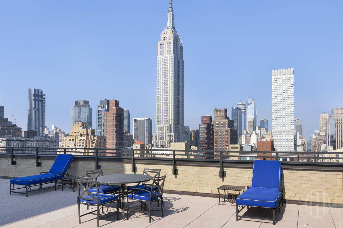 Rooftop terrace with blue lounge chairs and a Manhattan skyline view centered on the Empire State Building.