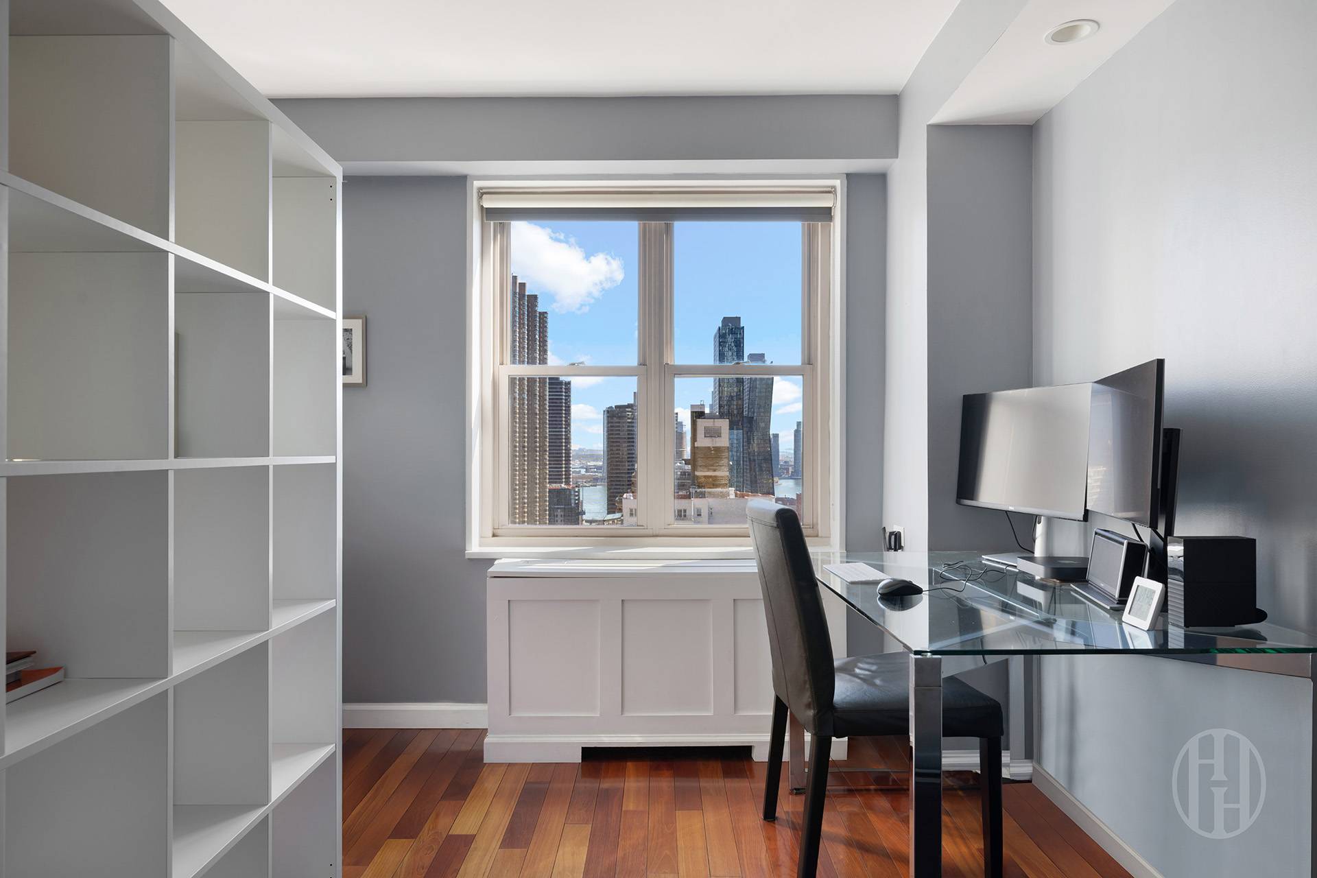 Home office with built-in shelving, glass desk, and a city-and-water view through the window.