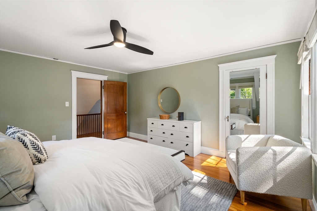 Bedroom with a white bed, sage-green walls, round mirror, and sunlit hardwood floor.