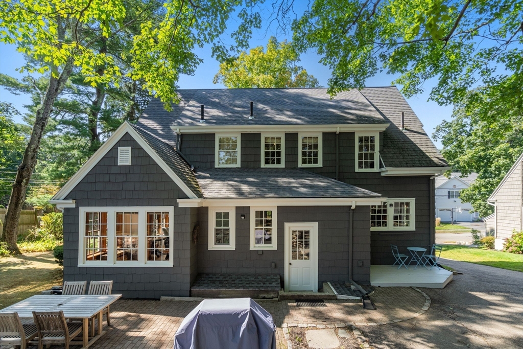 Rear of a dark shingle-sided house with a brick patio and outdoor dining furniture.