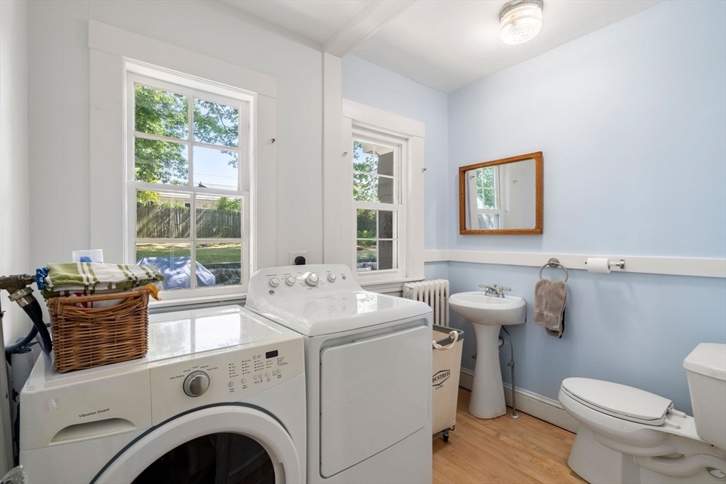 Laundry room with washer, dryer, pedestal sink, and toilet beneath large windows.