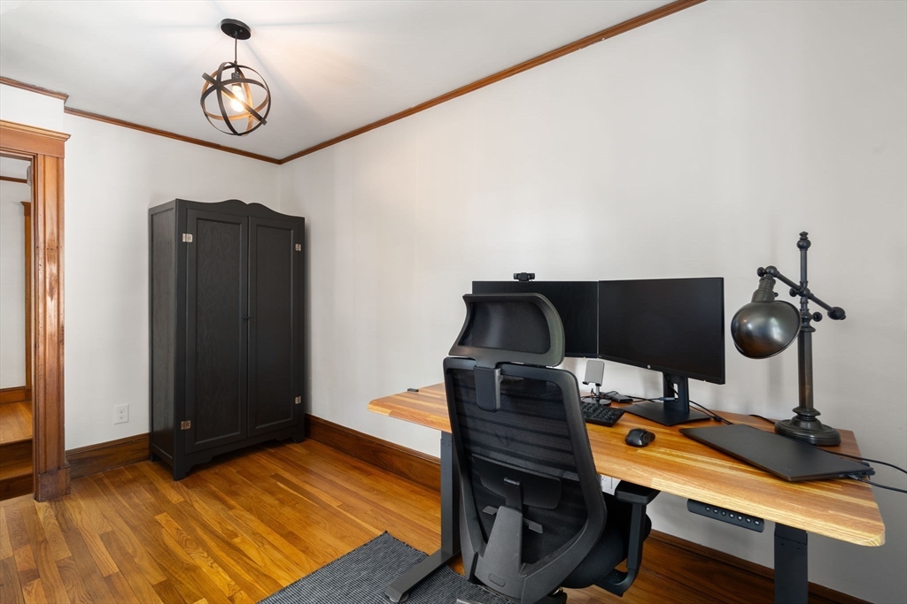 Home office with a wood desk, dual monitors, ergonomic chair, and hardwood floors.