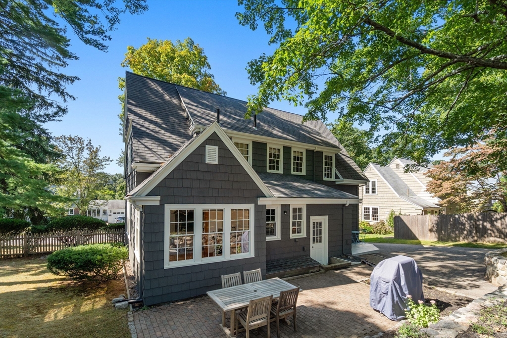 Rear of a dark shingle house with a brick patio, outdoor dining set, and covered grill.