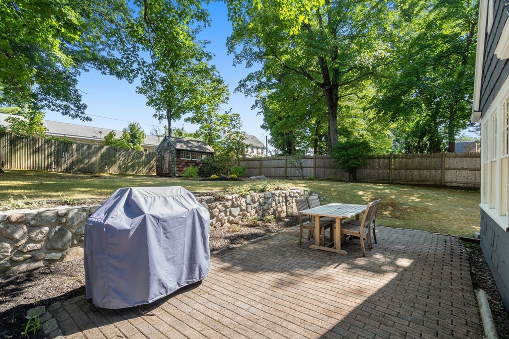 Backyard brick patio with a covered grill, outdoor dining set, stone wall, and fenced lawn.