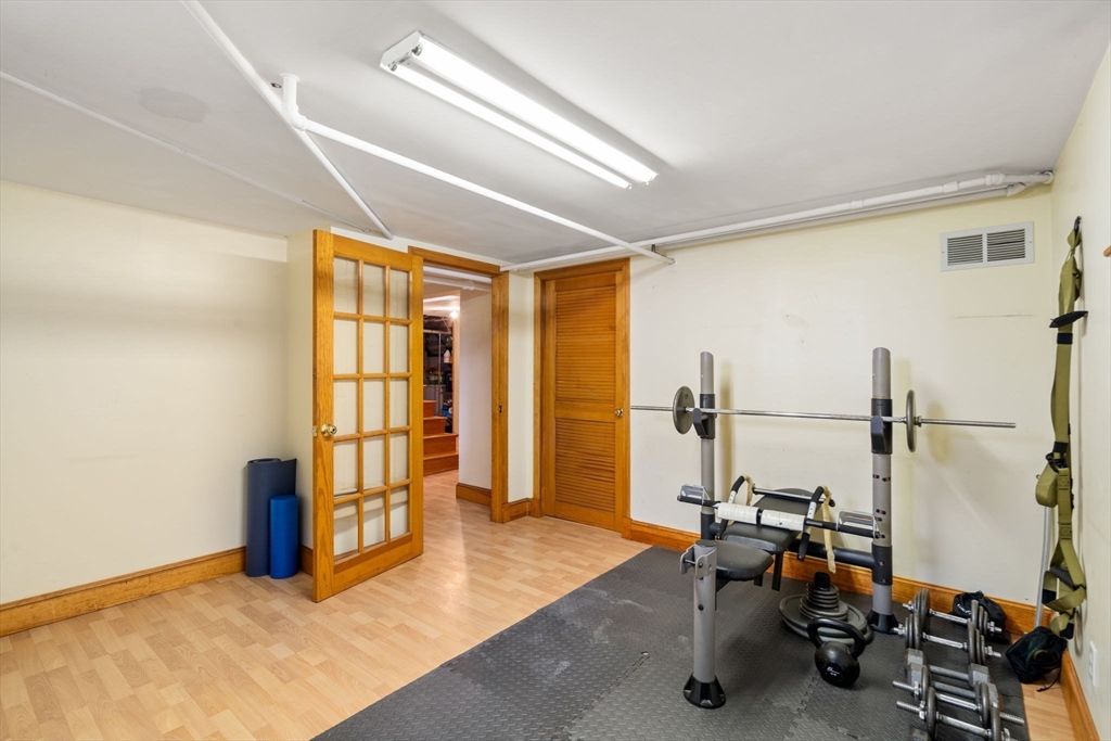 Home gym with weight bench, barbell, dumbbells, and an open glass-paneled door.