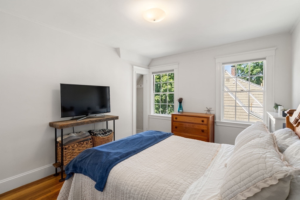 Bedroom with white bedding and blue throw, hardwood floors, and two sunlit windows.