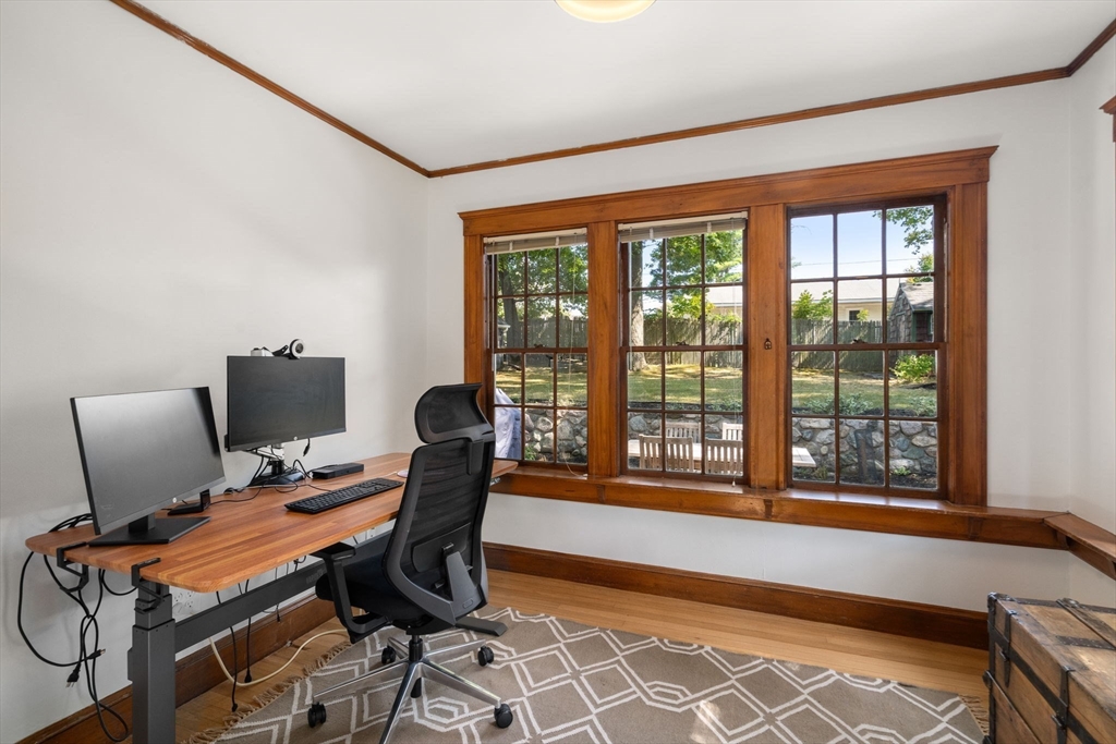Home office with a wood desk and monitors beside large wood-trimmed windows overlooking the backyard.