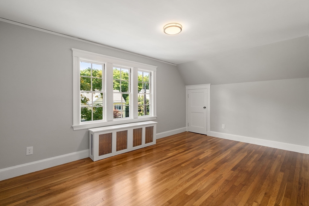 Empty bedroom with hardwood floors, three windows, and a sloped ceiling.